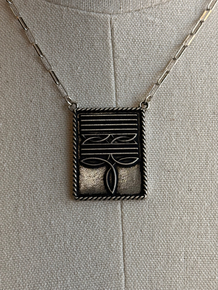 Rectangular boot-stitch pendant with engraved lines, shown on a chain