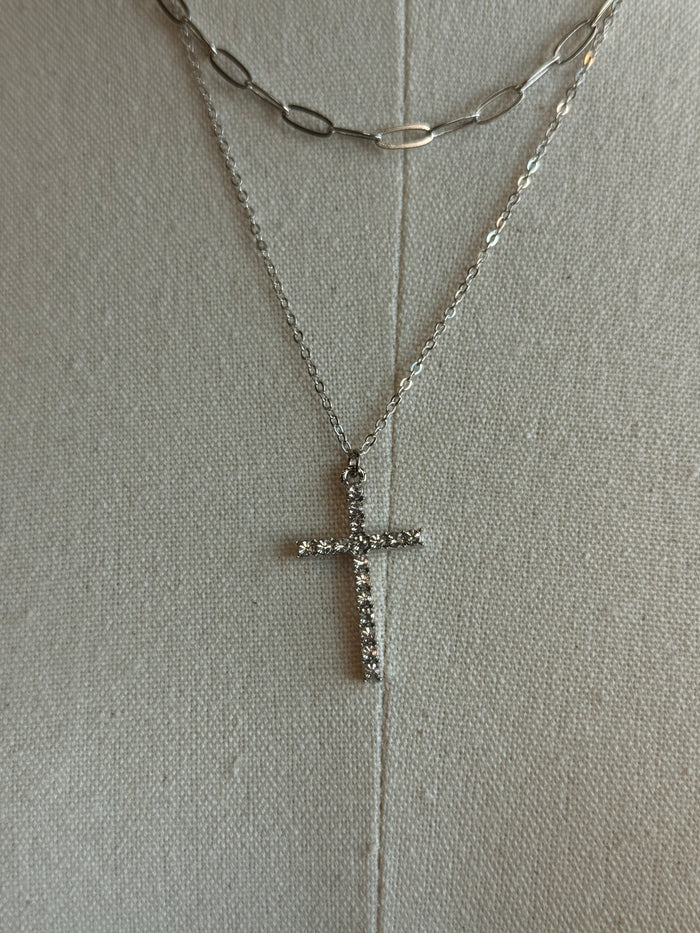 Close-up of silver cross pendant on stacked necklaces with chain details