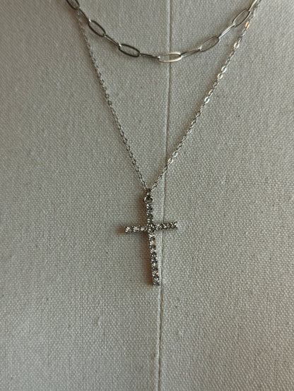 Close-up of silver cross pendant on stacked necklaces with chain details