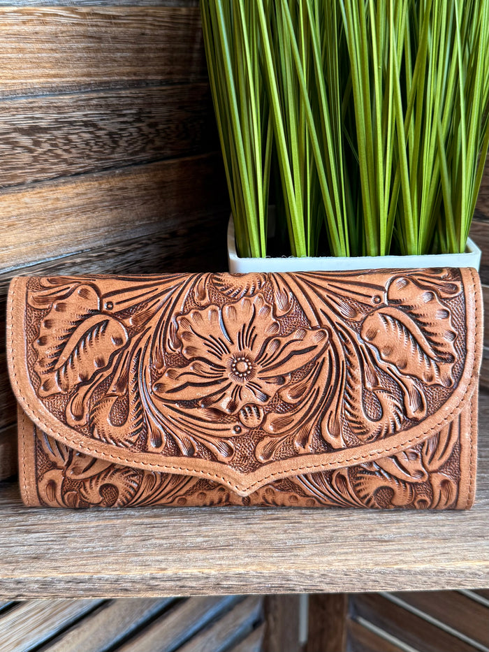 Carved brown leather flap wallet with floral tooling and snap button, front closed.