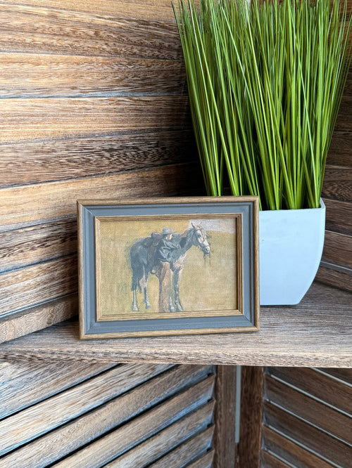 Framed cowboy and horse artwork with gray border frame on tabletop