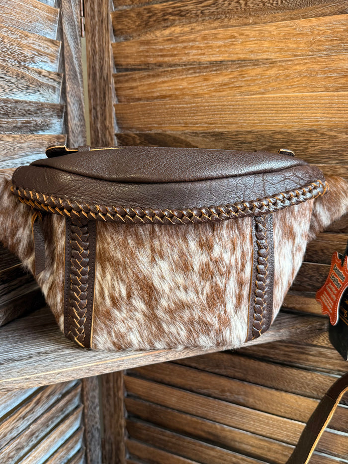 Hair-on cowhide sling bag with braided edge trim, brown flap top, and crossbody strap