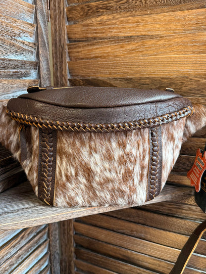 Hair-on cowhide sling bag with braided edge trim, brown flap top, and crossbody strap
