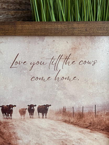 Close-up of framed wall art with handwritten quote over cow pasture landscape
