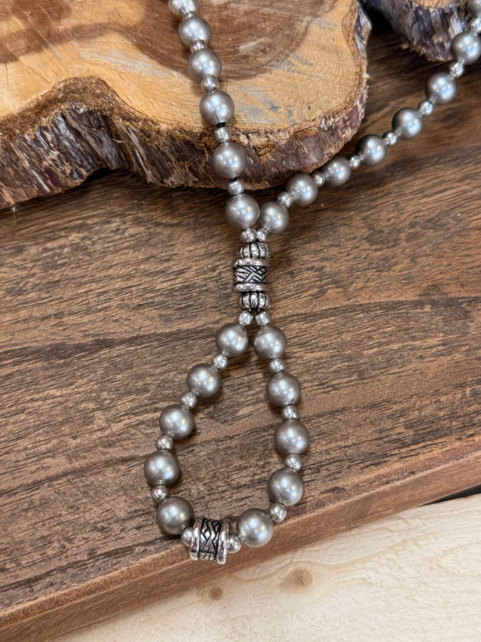 Close-up of loop pearl necklace with ornate bead detail and hanging tassel-like drops