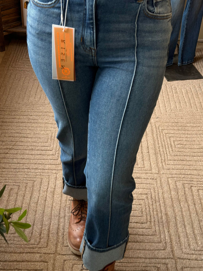 Close-up of cuffed medium-wash jeans with front seam and dark stitching accents.