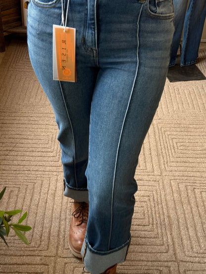 Close-up of cuffed medium-wash jeans with front seam and dark stitching accents.