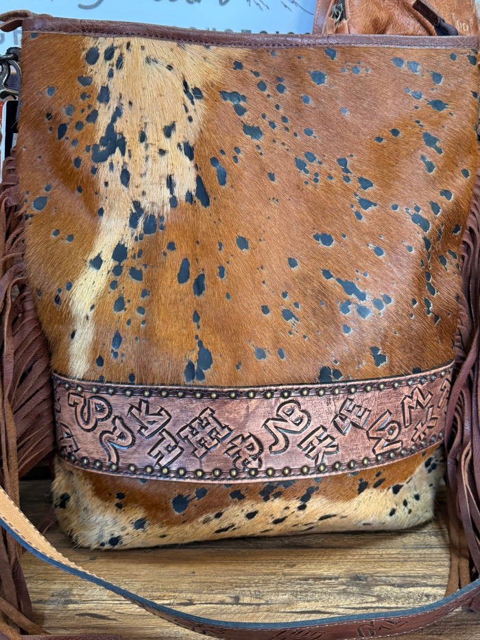 Fringed cowhide crossbody purse front flap with decorative stitched band and speckled hide
