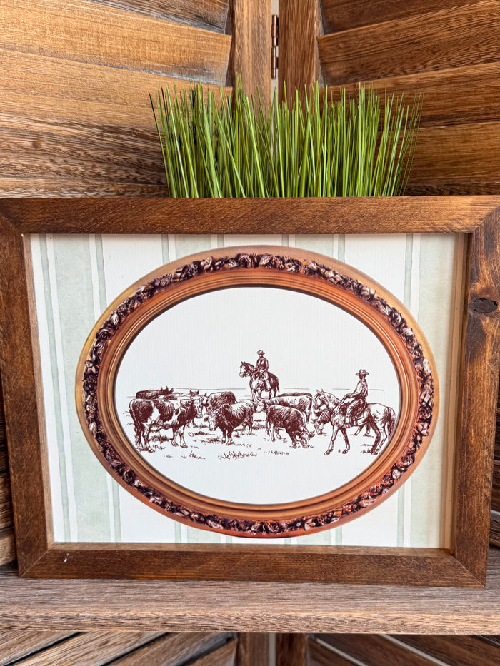 Framed cattle drive artwork with oval print, decorative inner border, and striped mat