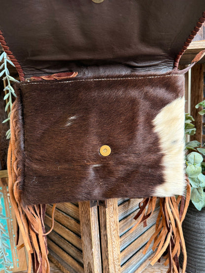 Fringed cowhide crossbody purse with solid front panel and small round gold snap