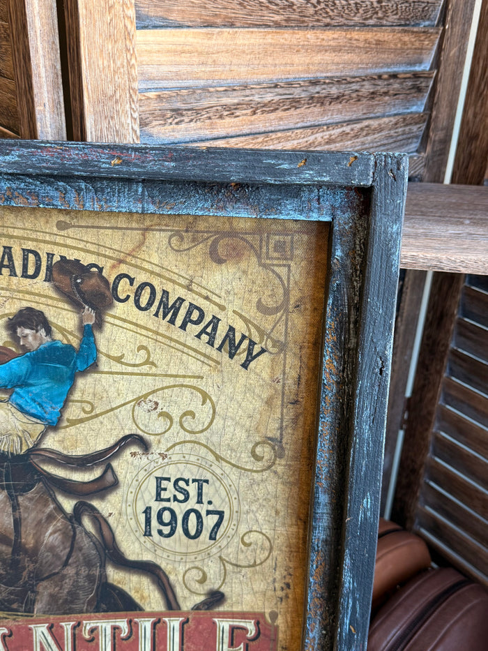 Close-up of vintage framed western artwork with blue rider and 'Est. 1907' badge