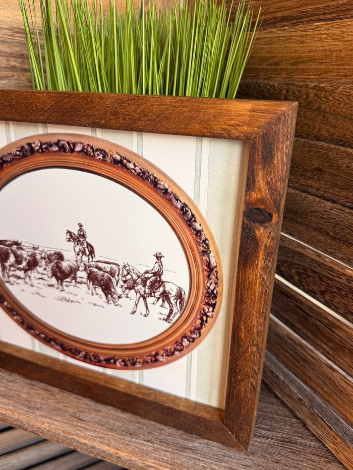 Close-up of framed oval cattle drive print with ornate decorative inner border