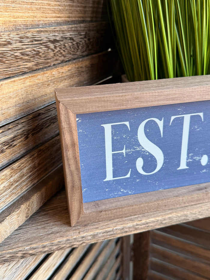 Framed “EST.” wall artwork corner view, blue panel with light wood frame, 12x4