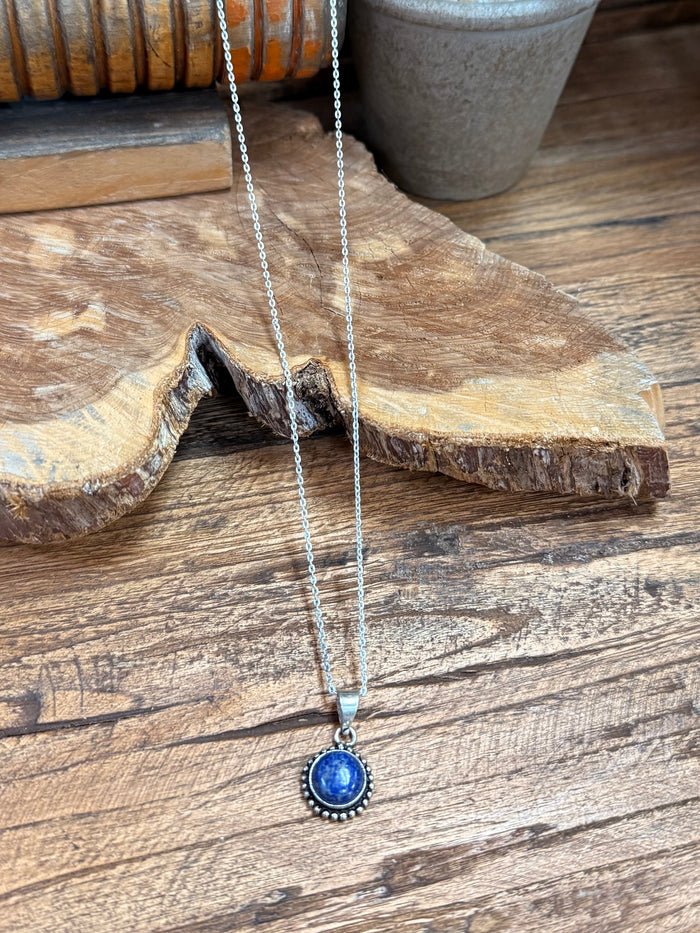Lapis-blue round pendant on silver chain, detailed bezel and halo edge