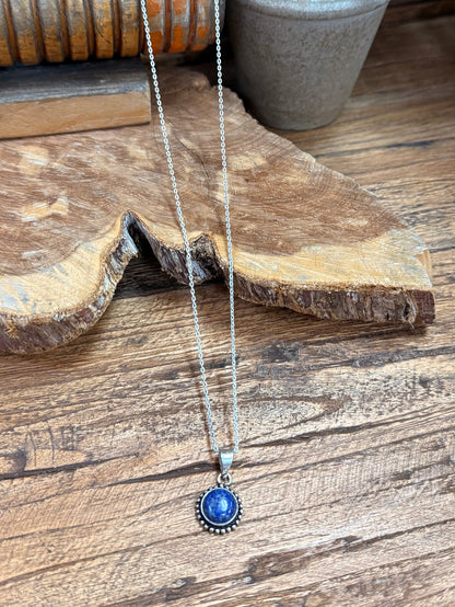 Lapis-blue round pendant on silver chain, detailed bezel and halo edge