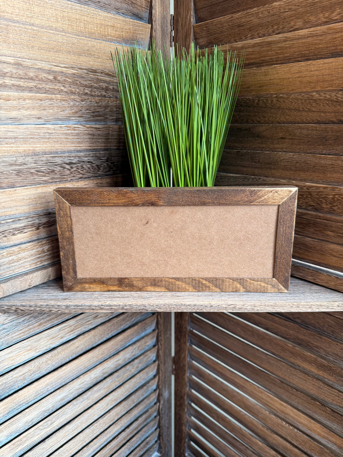 Wood framed panel with blank center and green grass-like decoration in planter