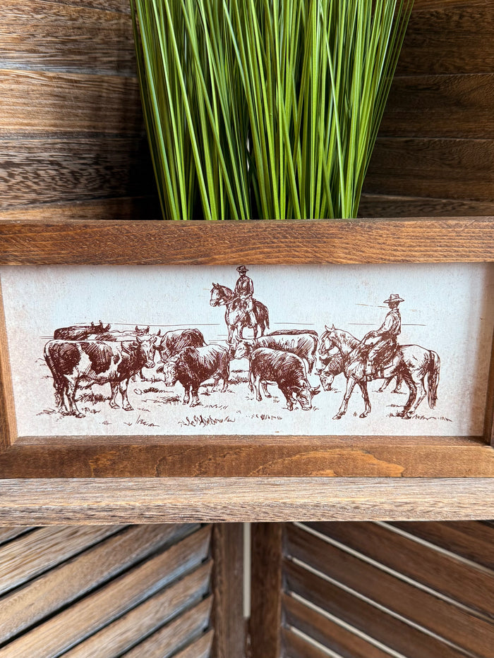 Wood framed cattle drive print showing cowboys on horseback and a herd of cattle