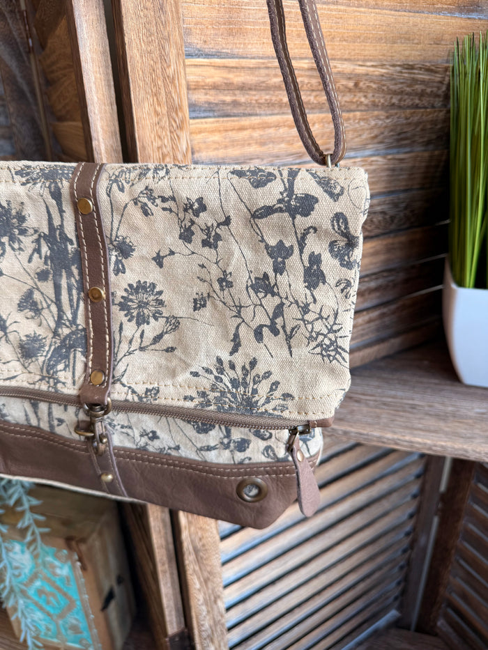 Canvas flap crossbody bag with blue floral print, brown leather trim, and snap pocket