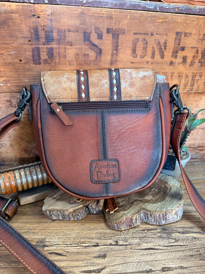 Brown cowhide flap crossbody bag with front flap pocket, top zipper, and side strap hardware