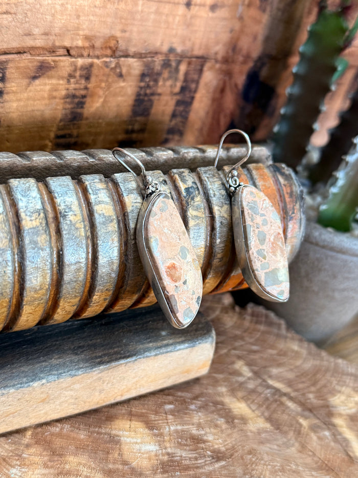 Angled view of oval jasper drop fishhook earrings with silver-tone hooks and mottled finish