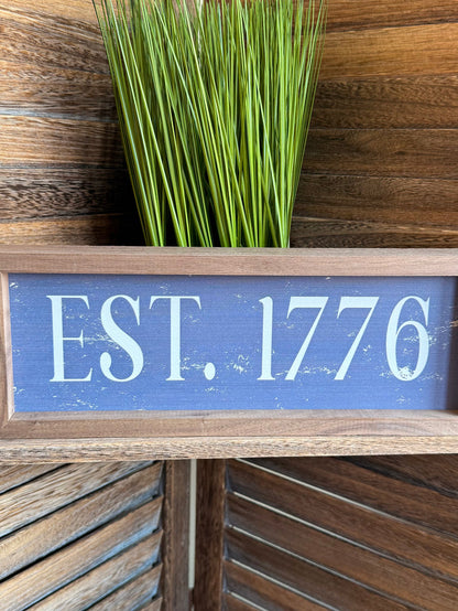 Framed “EST. 1776” wall artwork, close view of blue text and light wood frame, 12x4