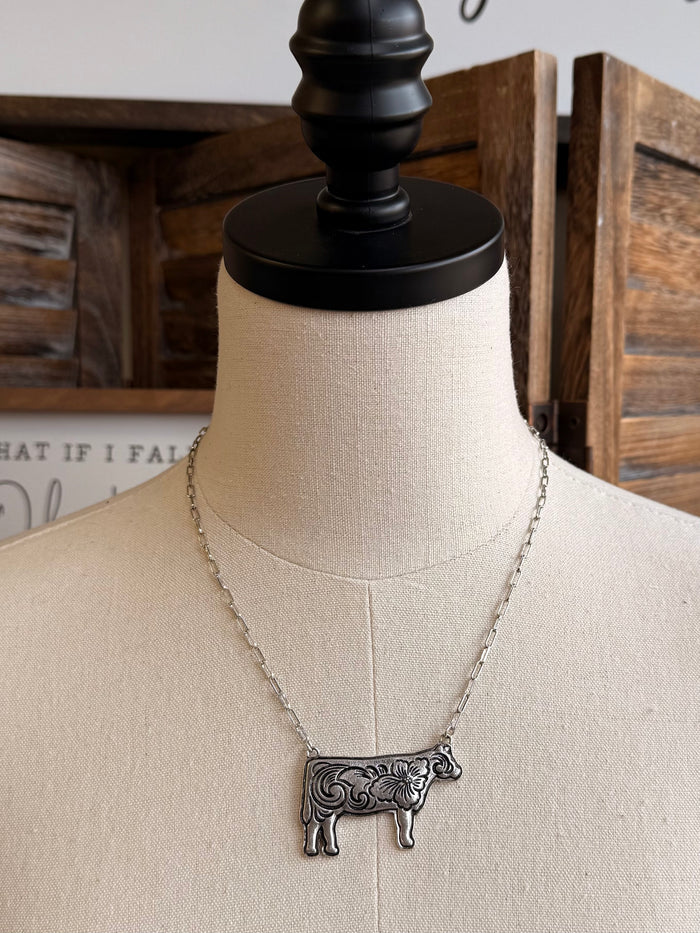 Silver-tone cow pendant necklace with ornate filigree, shown on bust