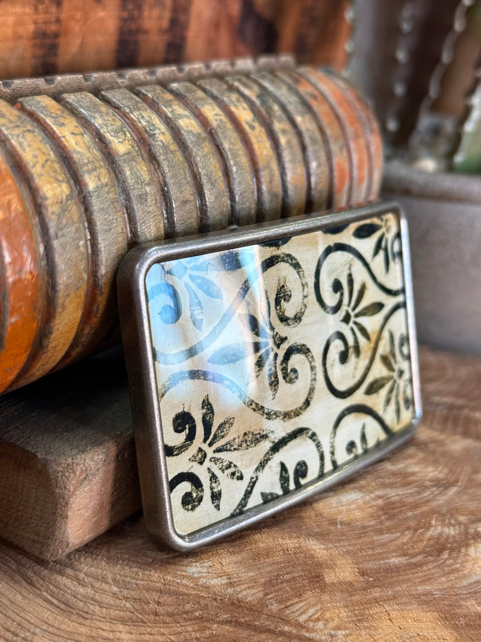 Silver belt buckle with black-and-blue floral scroll design, angled view