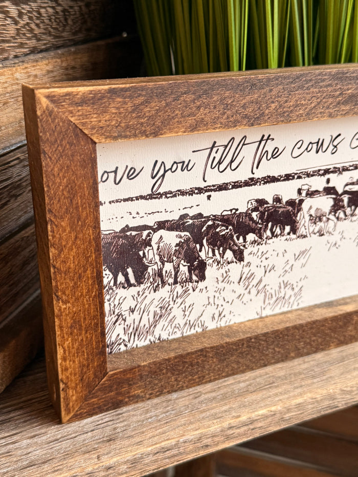 Wood-framed black-and-white cow herd artwork with oversized cursive text