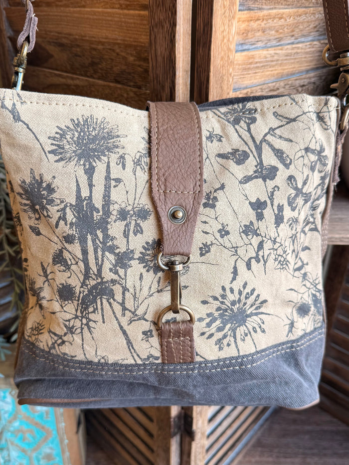 Floral canvas crossbody bag front panel with brown center strap and metal snap detail
