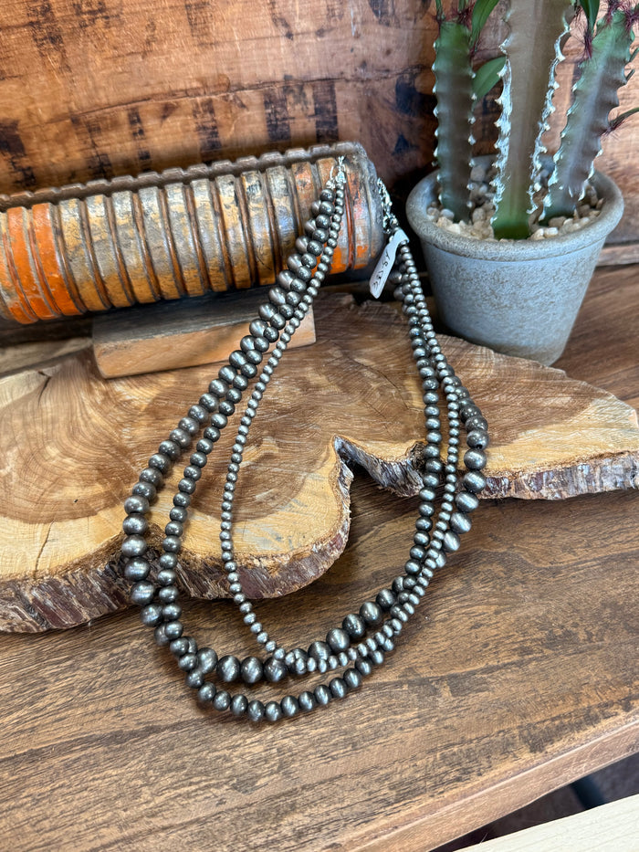 Triple-strand beaded necklace with dark metallic pearls and arrowhead pendant