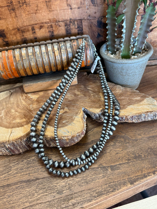 Triple-strand beaded necklace with dark metallic pearls and arrowhead pendant
