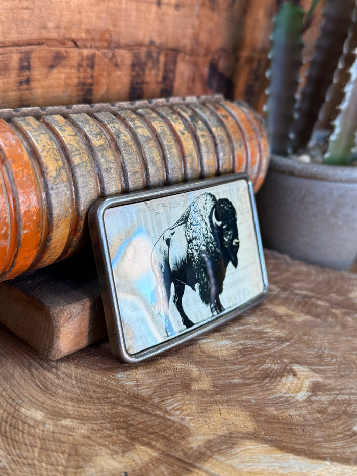 Rectangle belt buckle with buffalo graphic on metal frame, angled on wooden surface