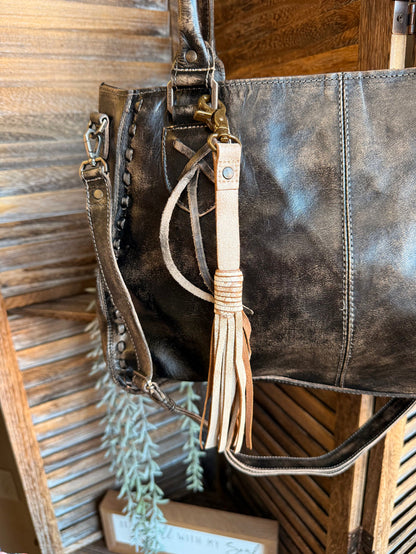 Leather tote with a light tan tassel clip and braided hanging fringe