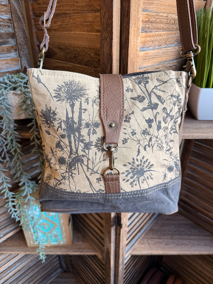 Floral canvas crossbody bag with brown leather trim, blue print, and snap top closure