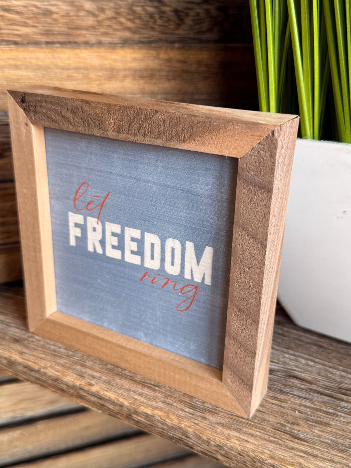 Angled wooden 4x4 framed artwork with blue panel and “Let FREEDOM ring” text