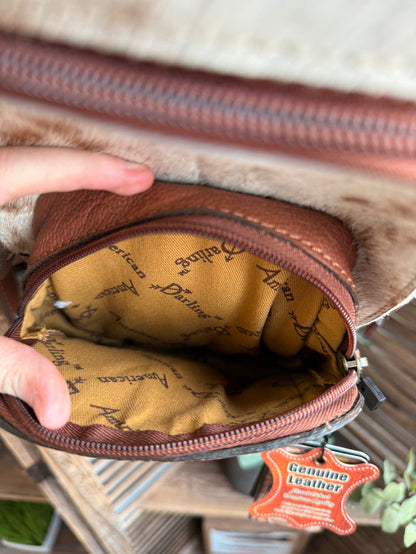 Inside hair-on sling backpack with tan logo-pattern lining and zipper pocket