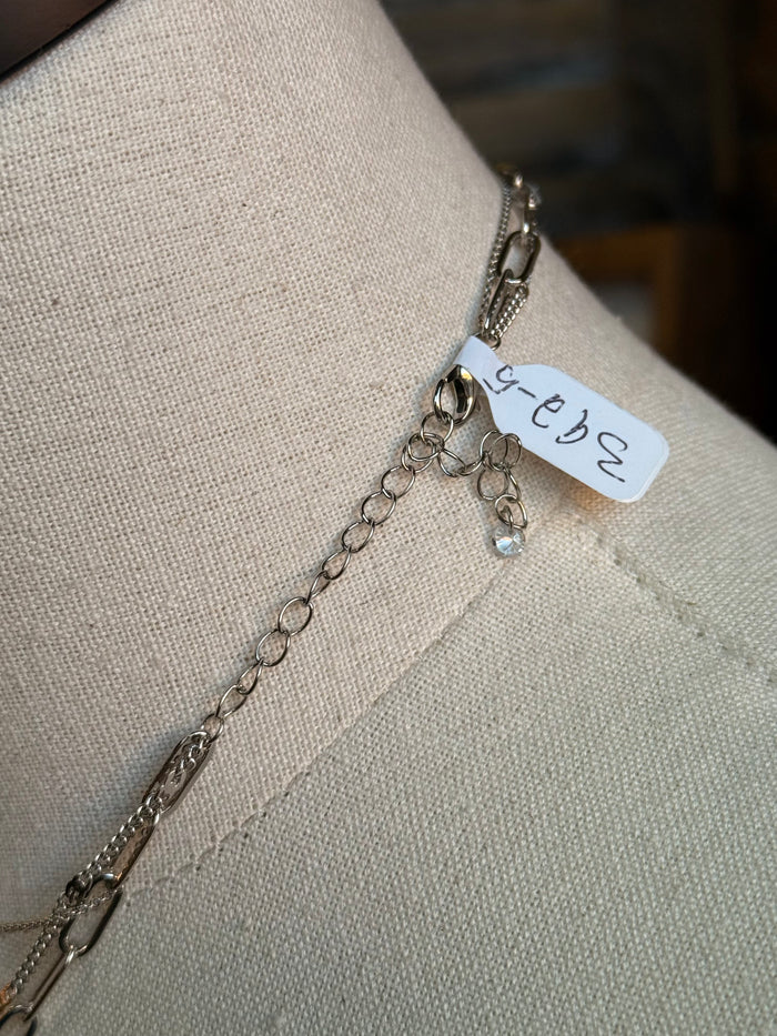 Silver chain necklace with rectangular pendant and small engraved tag on a short extender