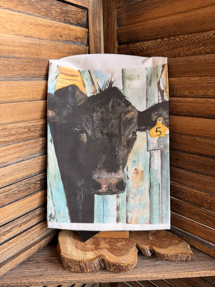 Watercolor cow tea towel with black cow face and yellow tag marked 5