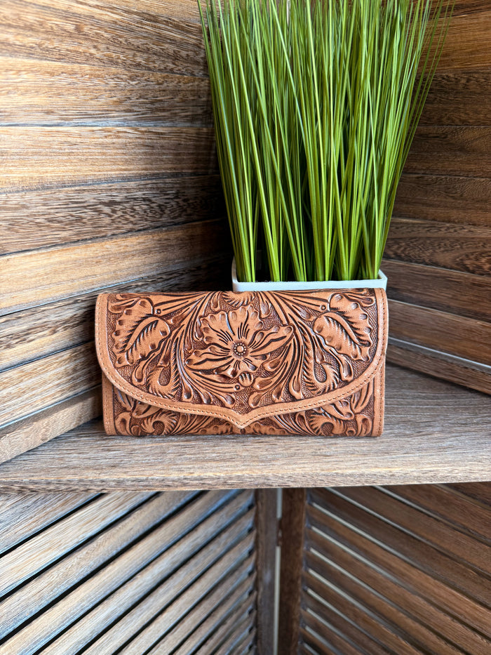 Brown carved leather flap wallet with floral tooling and round metal snap, front view.