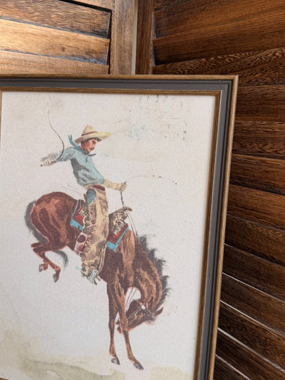 Framed cowboy on bucking bronco print, dark wood frame, angled view
