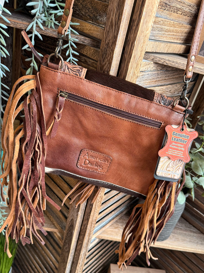 Brown leather crossbody purse with long fringe, zip pocket, and brand patch on front