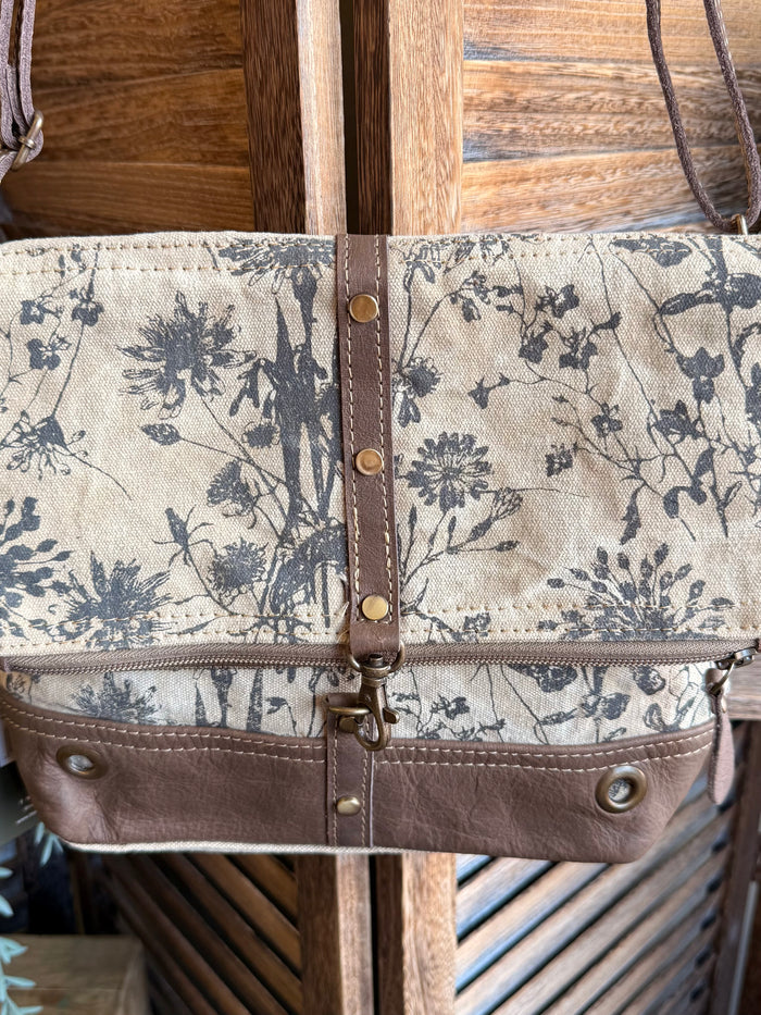 Flap canvas bag with blue floral pattern, riveted brown strap and front snap bar