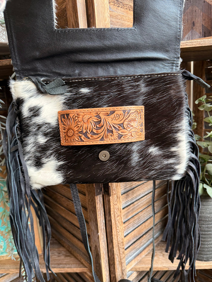 Black leather crossbody clutch with cowhide front panel, snap closure, and black fringe