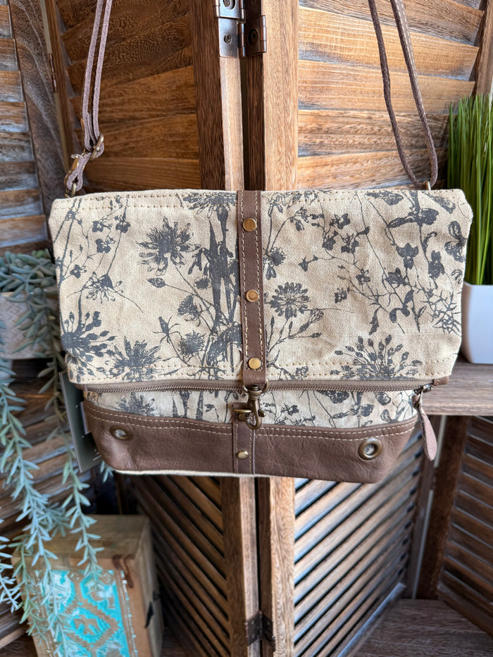 Flap canvas bag with blue floral print, brown leather trim, and front snap closure