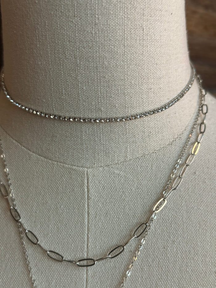 Silver layered necklace chains with linked details around a mannequin neck