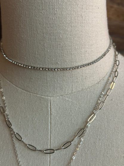Silver layered necklace chains with linked details around a mannequin neck