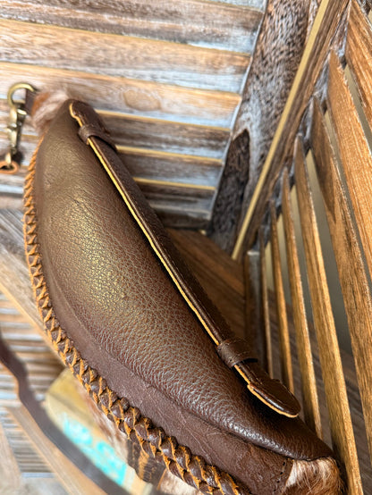 Brown leather sling bag with braided trim, brass clasp, and adjustable crossbody strap
