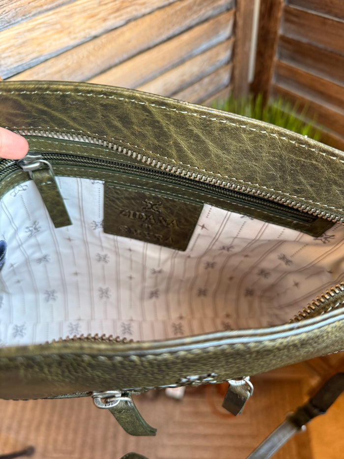 Olive leather crossbody bag interior with zip top, logo label, and patterned lining.