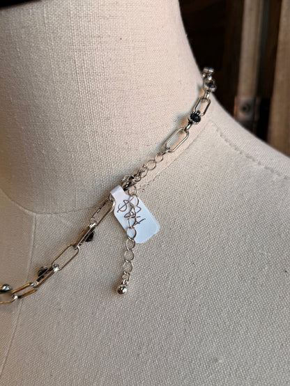 Detail of chunky silver chain necklace with dangling links and black stone beads