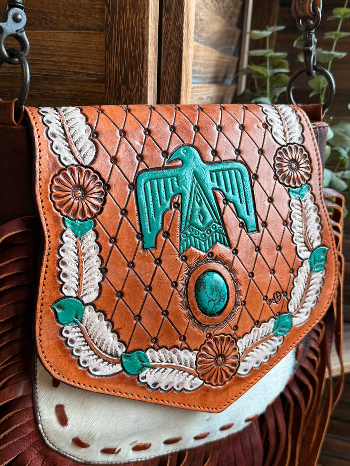 Fringed cowhide crossbody purse with teal Thunderbird graphic and floral border stitching